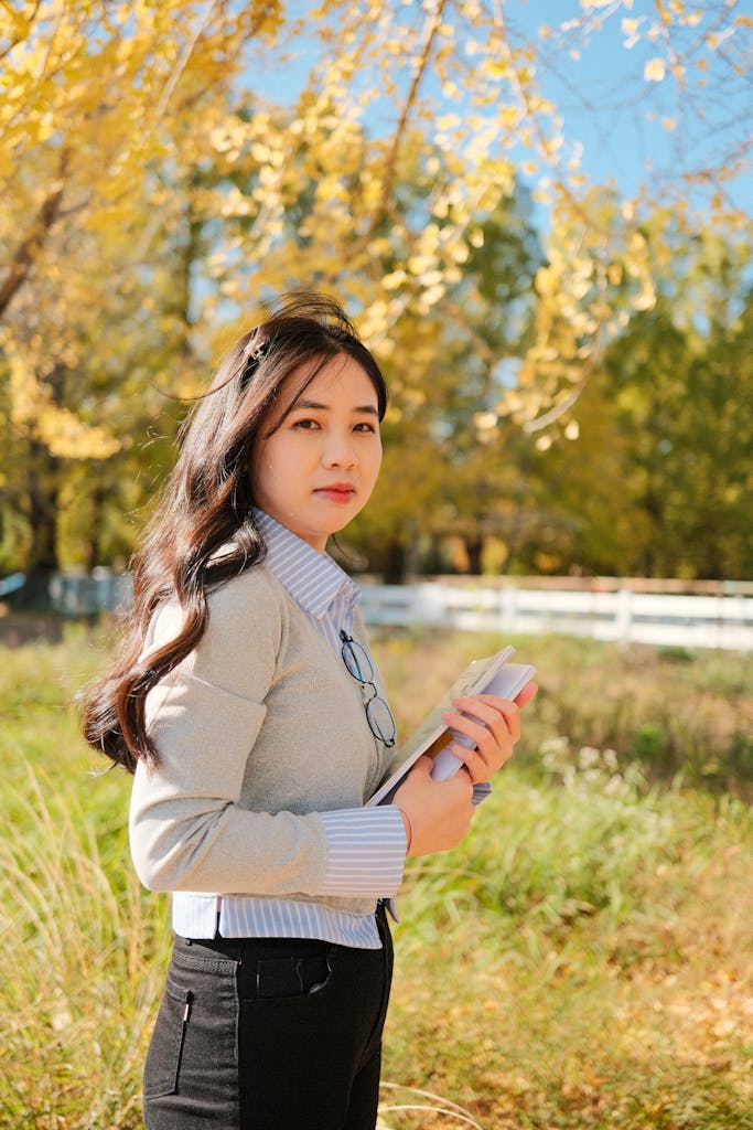 Young woman in a sunny autumn park holding books. Perfect for lifestyle and educational themes.
