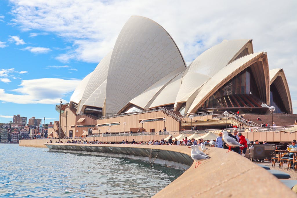 Sydney Opera House with tourists and waterfront view on a sunny day.